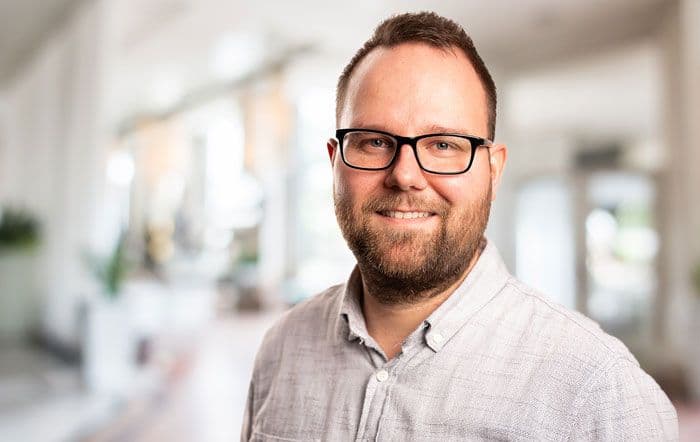 Ein freundlicher Mann mit Bart, Brille und weißem Hemd.