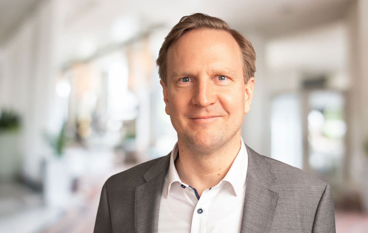 Freundliches Porträt von David Kopka, Ansprechpartner im Außendienst. Lächelnder Mann im Anzug, in einem modernen Büroambiente.