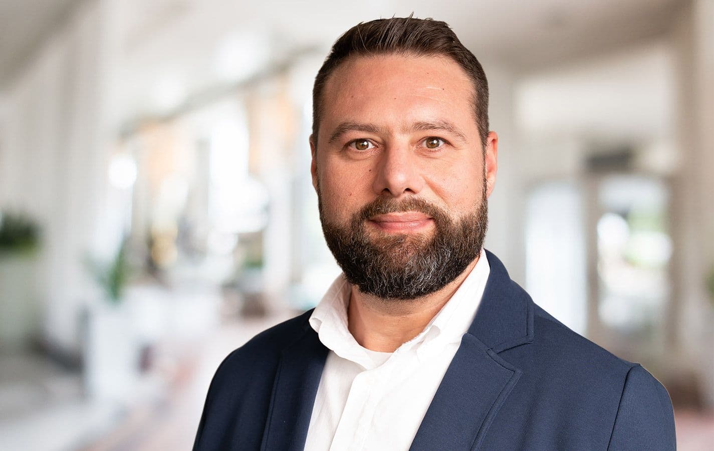 Ein freundlicher Mann mit Bart, dunklem Anzug und weißem Hemd.