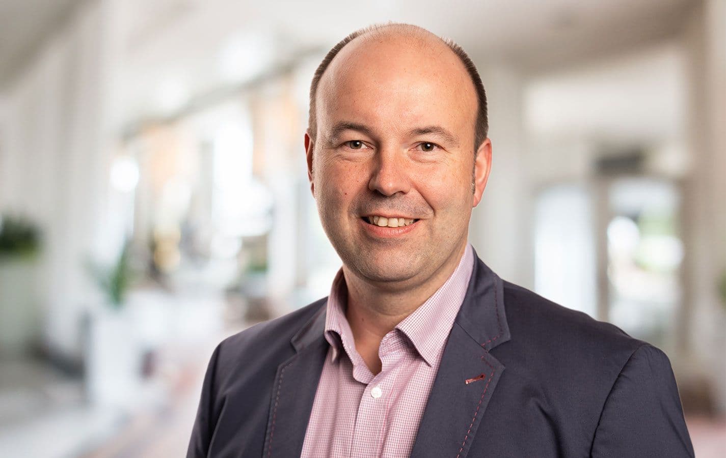 Freundliches Porträt von Marco Schröder, Ansprechpartner im Außendienst. Lächelnder Mann im Anzug, in einem modernen Büroambiente.