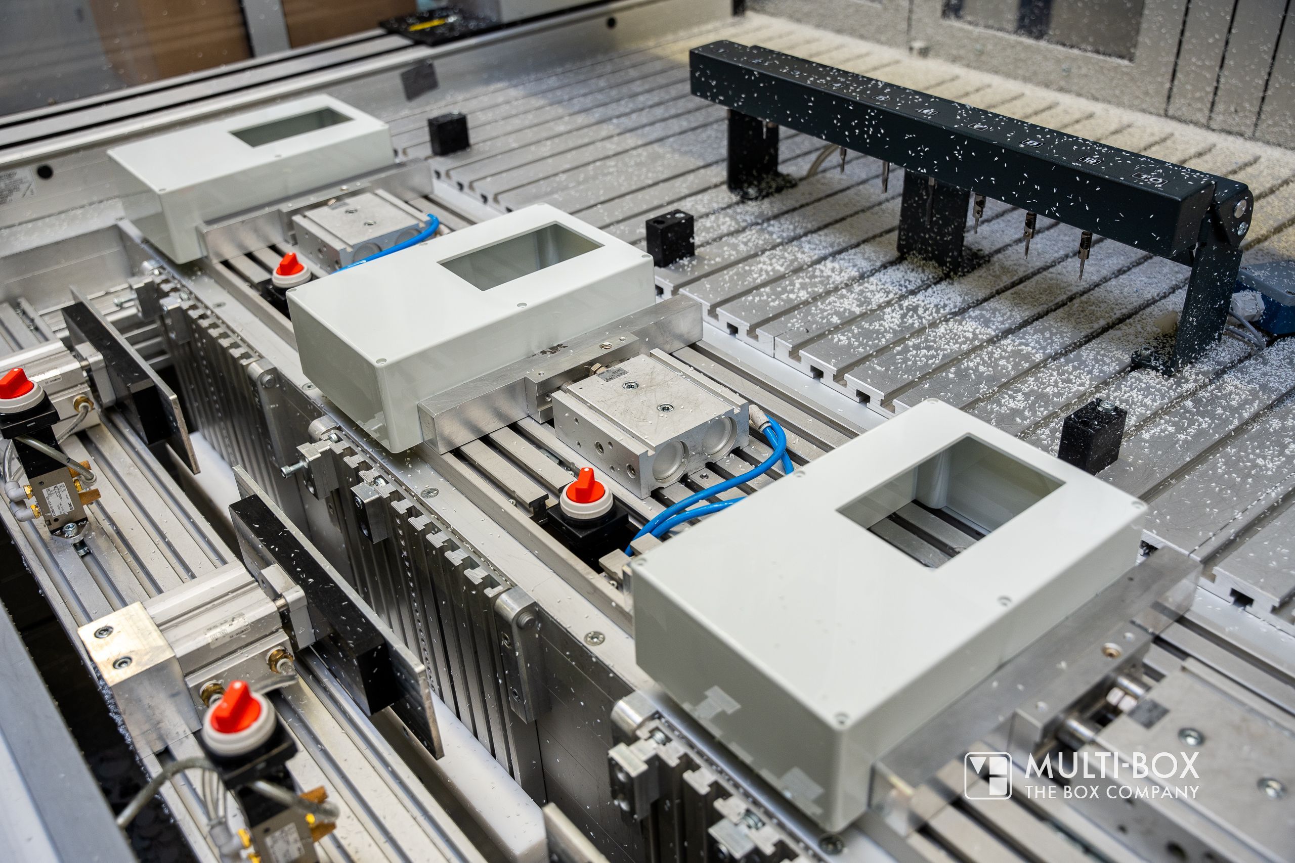 A CNC machine processes aluminum enclosures positioned precisely on the table.