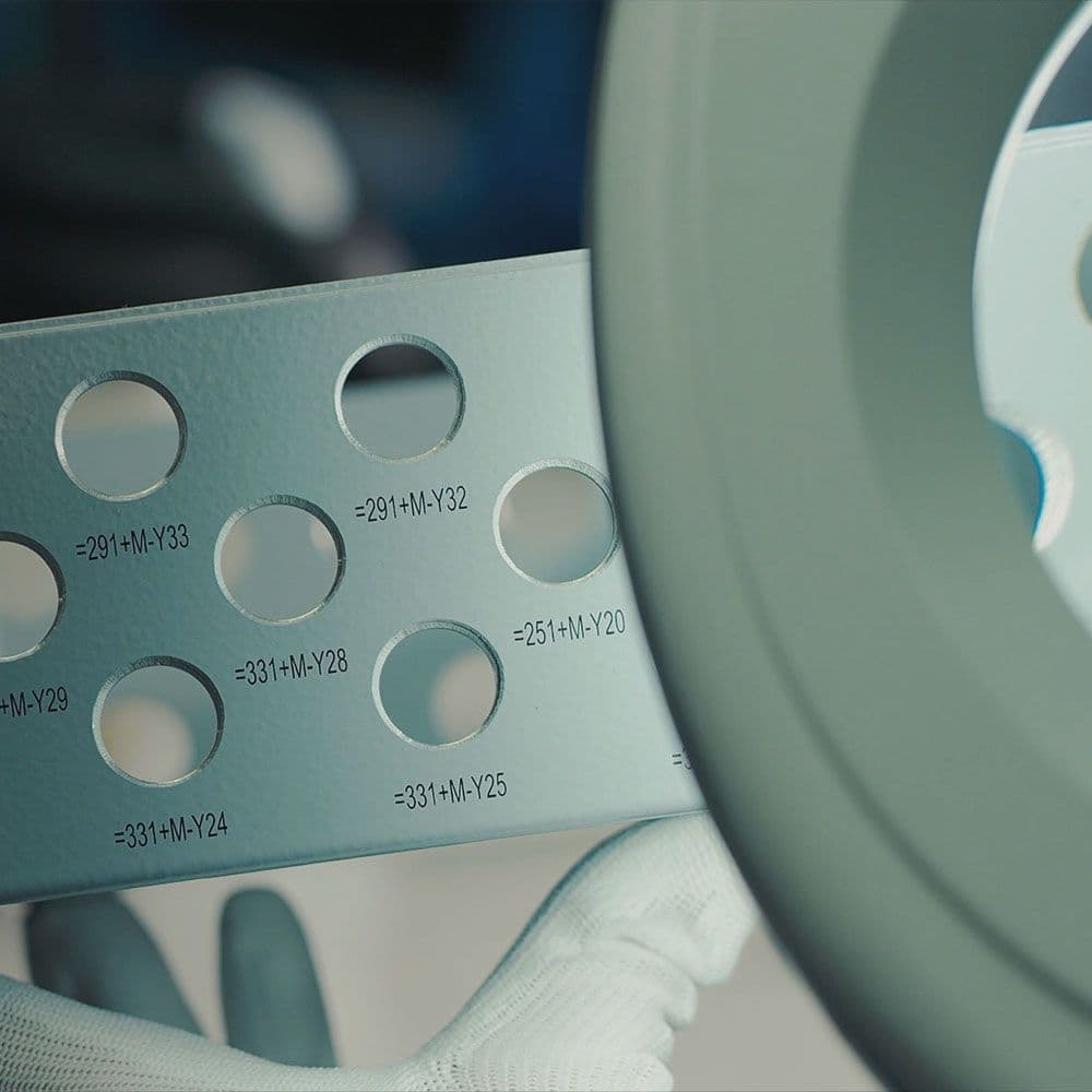 A technician inspects a metal enclosure with drilled holes and precise markings during quality control.